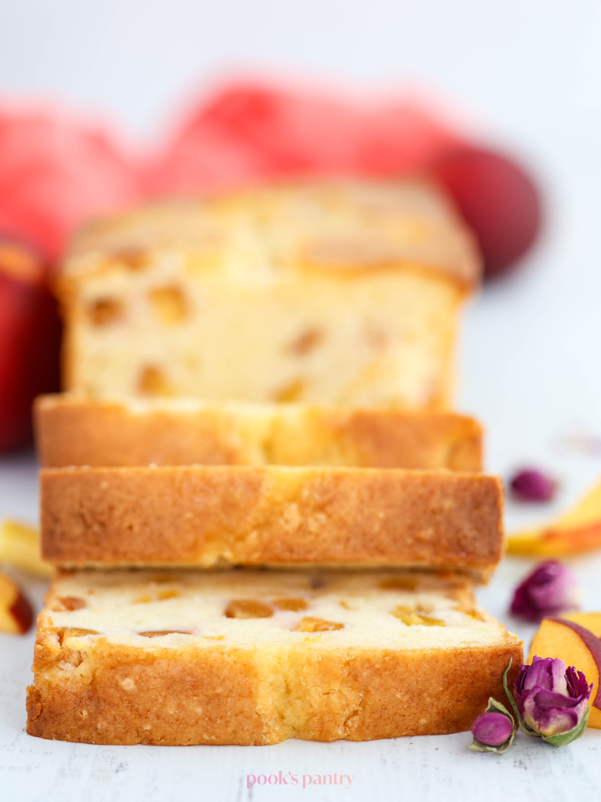 Sliced pound cake with dried rose buds and sliced peaches on the side of the cake.