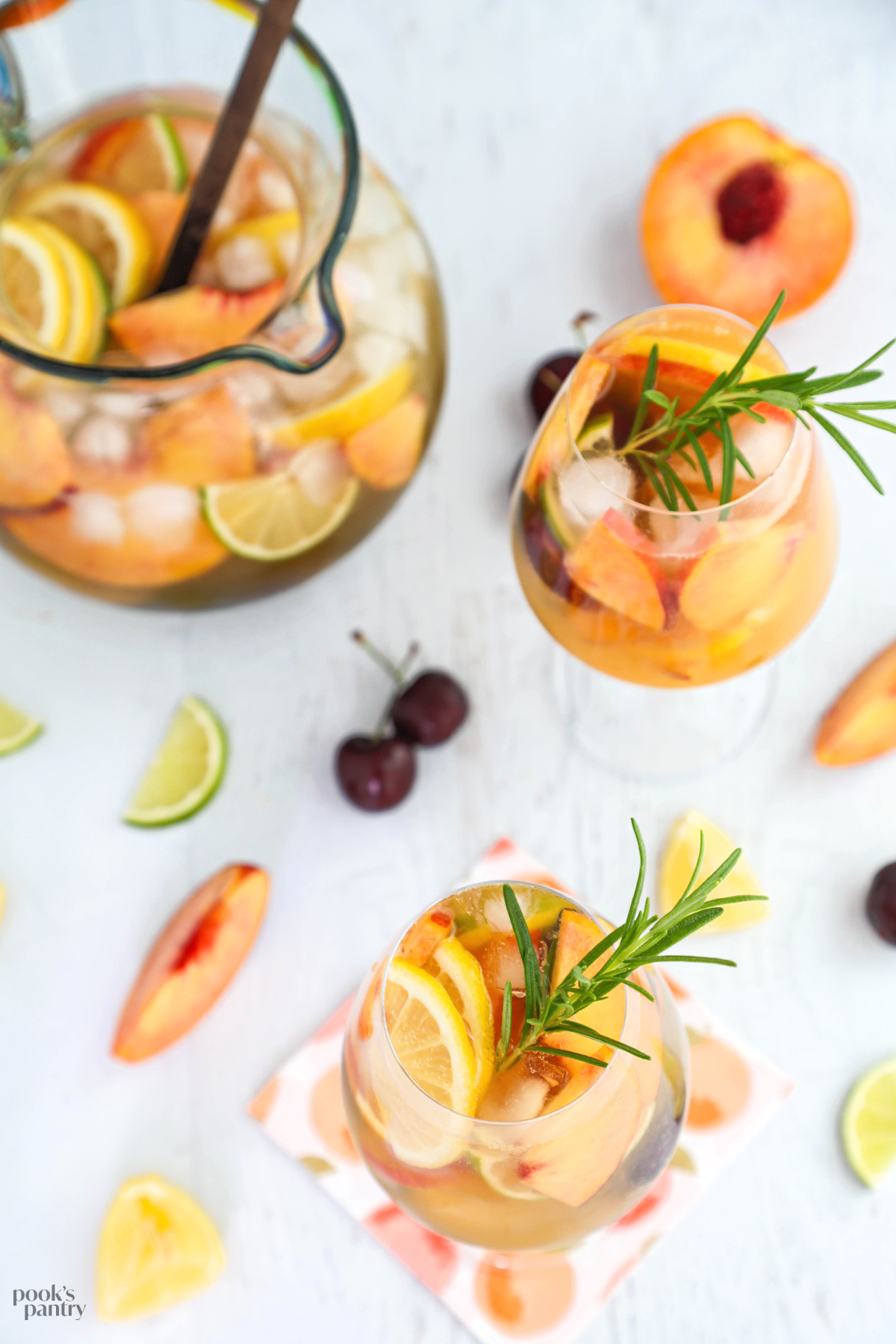 Overhead photo of glasses of peach sangria with the pitcher in the background. There is fruit scattered around the base of the glasses.