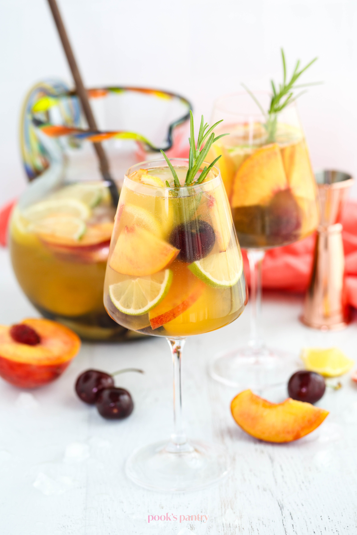 White wine peach sangria in glasses garnished with rosemary and fresh fruit.