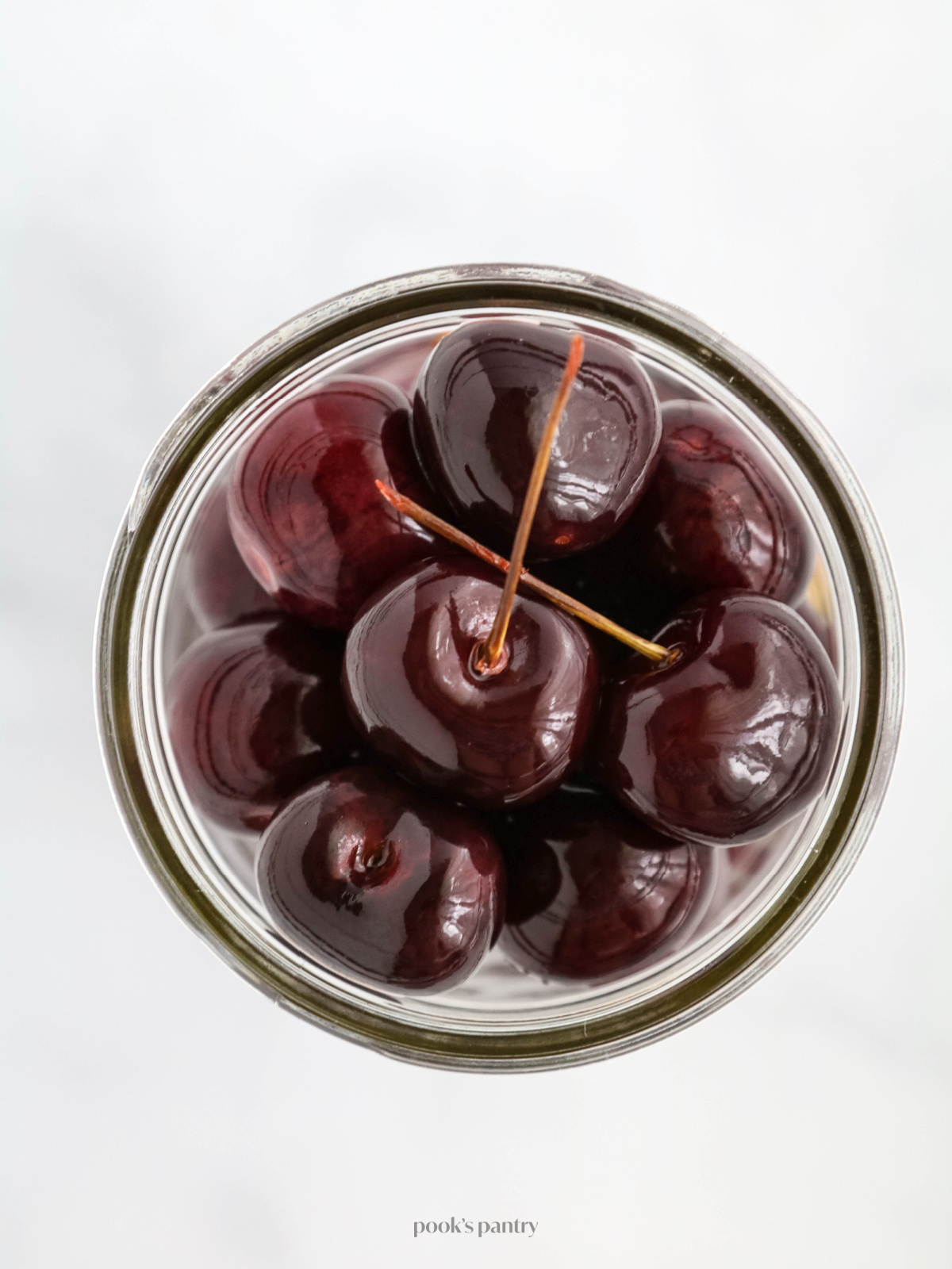 Overhead photo of pickled cherries in a glass canning jar on a white background.