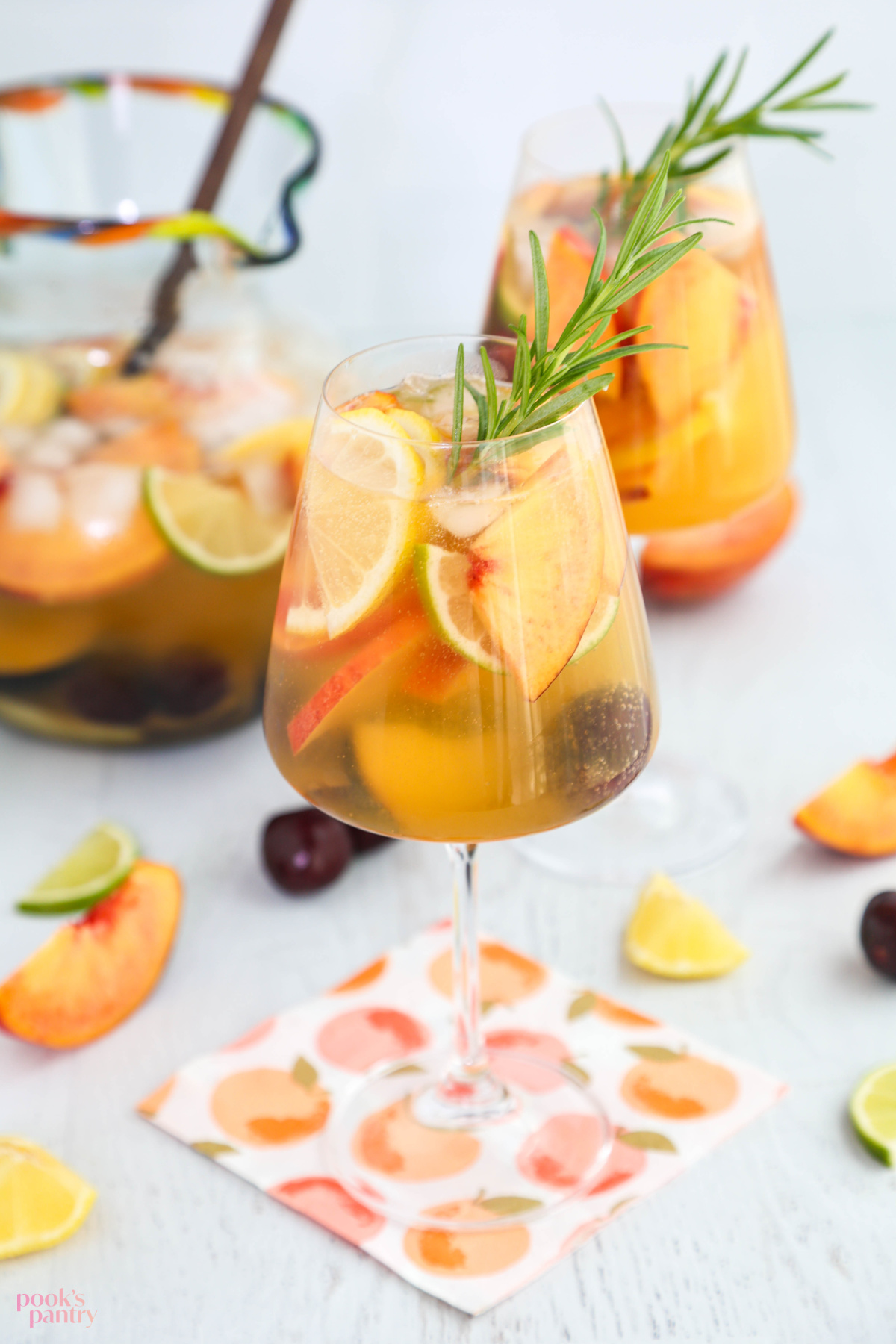 Glasses of white wine sangria with fruit and a sprig of rosemary on a white background.