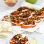 Two pieces of apple chutney bruschetta on a small white plate, with a platter of crostini in the background.