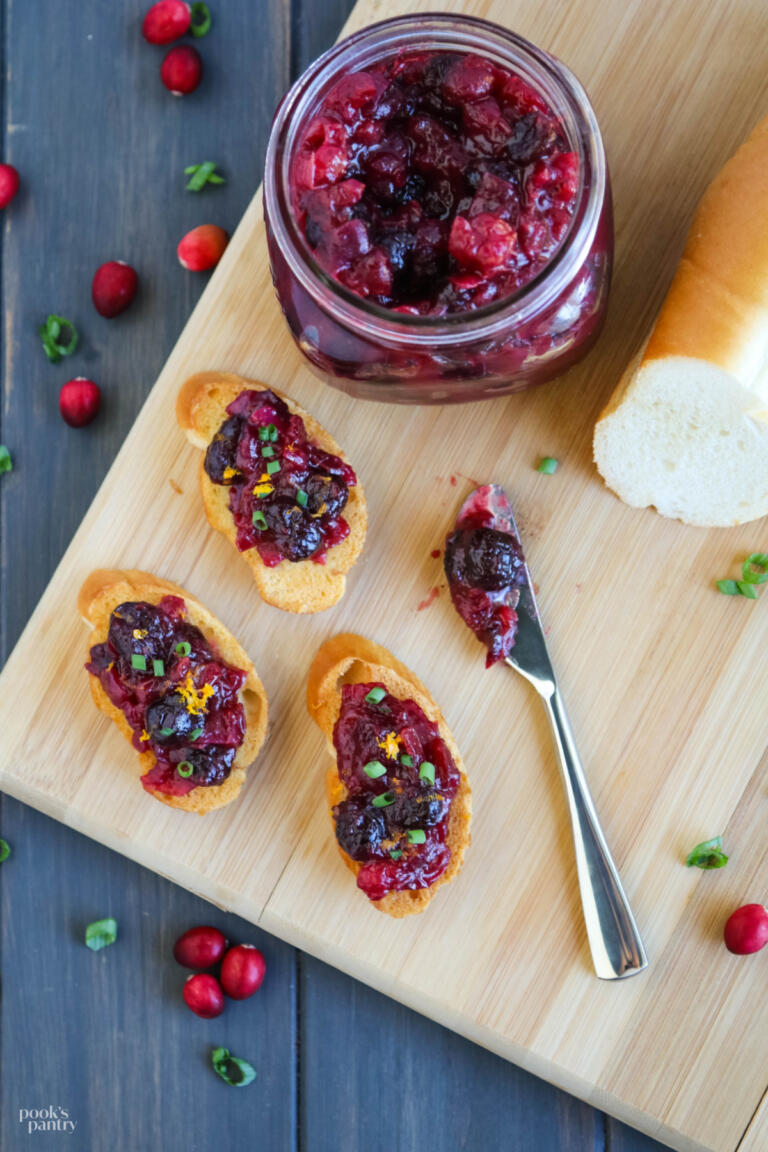 Cranberry chutney on toasted baguette slices on a wooden cutting board.