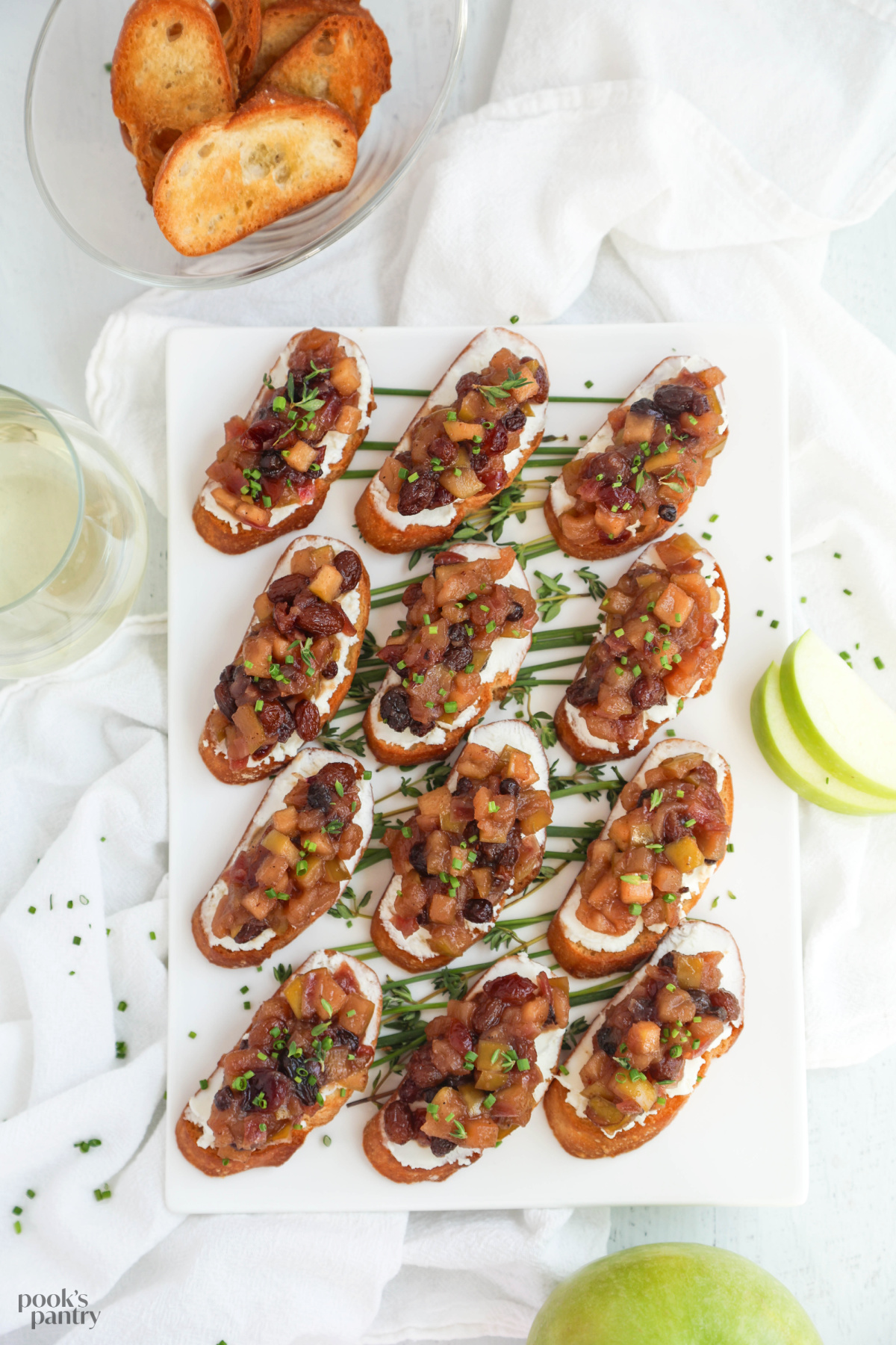 An overhead photo of a platter of apple bruschetta with a bowl of crostini in the top corner.