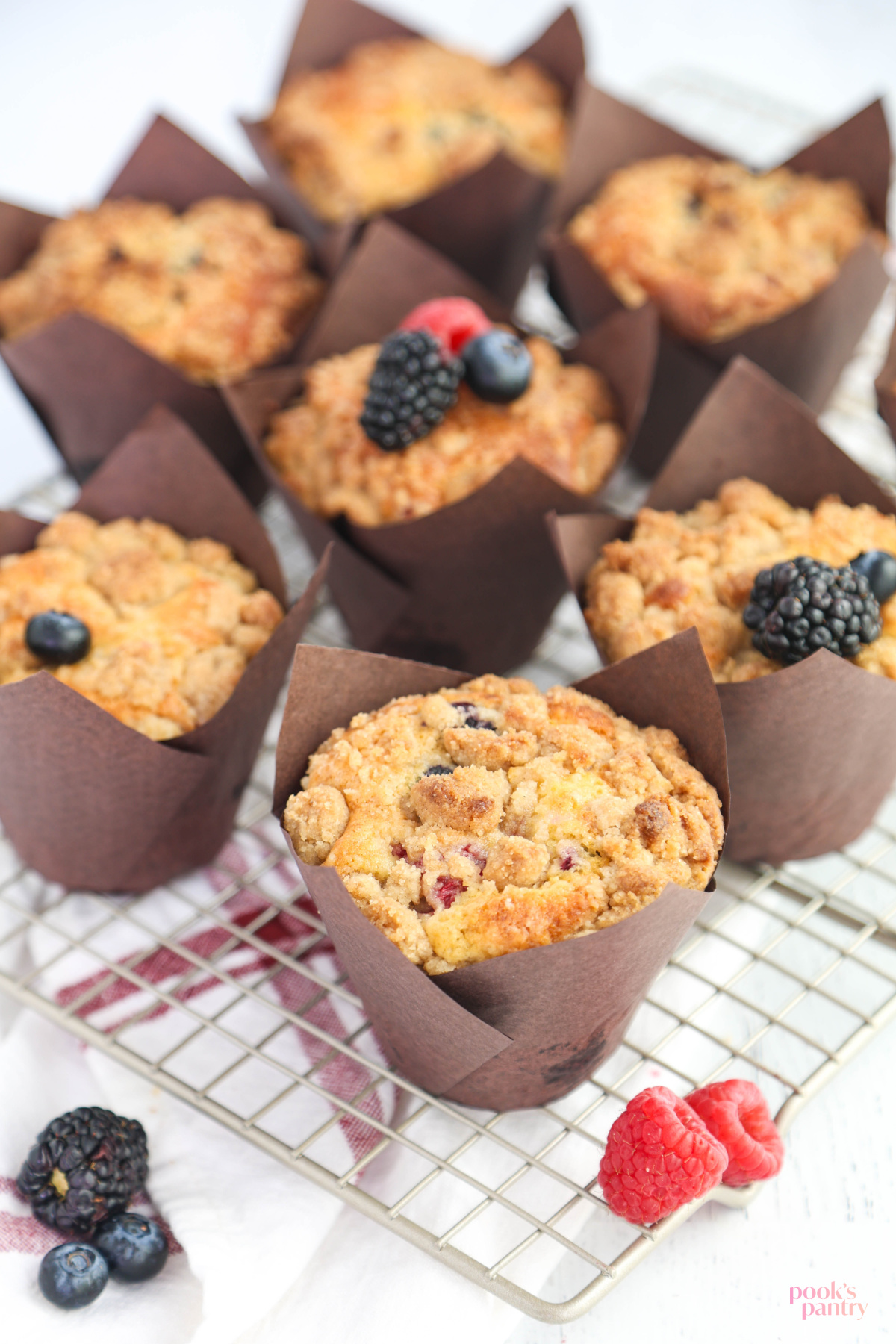 Triple berry muffins on metal cooling rack with a few berries scattered around.