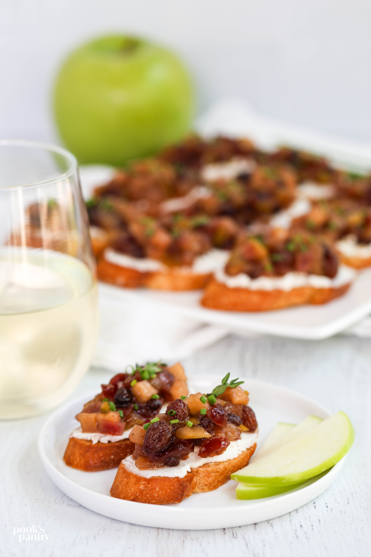 Apple chutney bruschetta with goat cheese on toasted baguette, with sliced apple on the side.