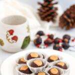 Buckeye balls in paper dessert cups on a small white plate. There is a handmade pottery cup and a buckeye necklace in the background.