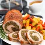 Chestnut stuffed pork loin recipe on a white platter, with roasted root vegetables on the side.