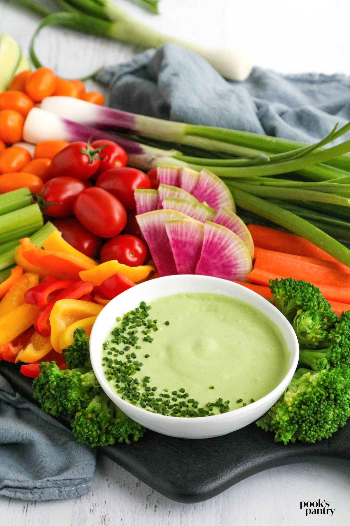 An assortment of fresh vegetables with a bowl of creamy goat cheese buttermilk herb dip to make a crudite board for a fall appetizer spread.