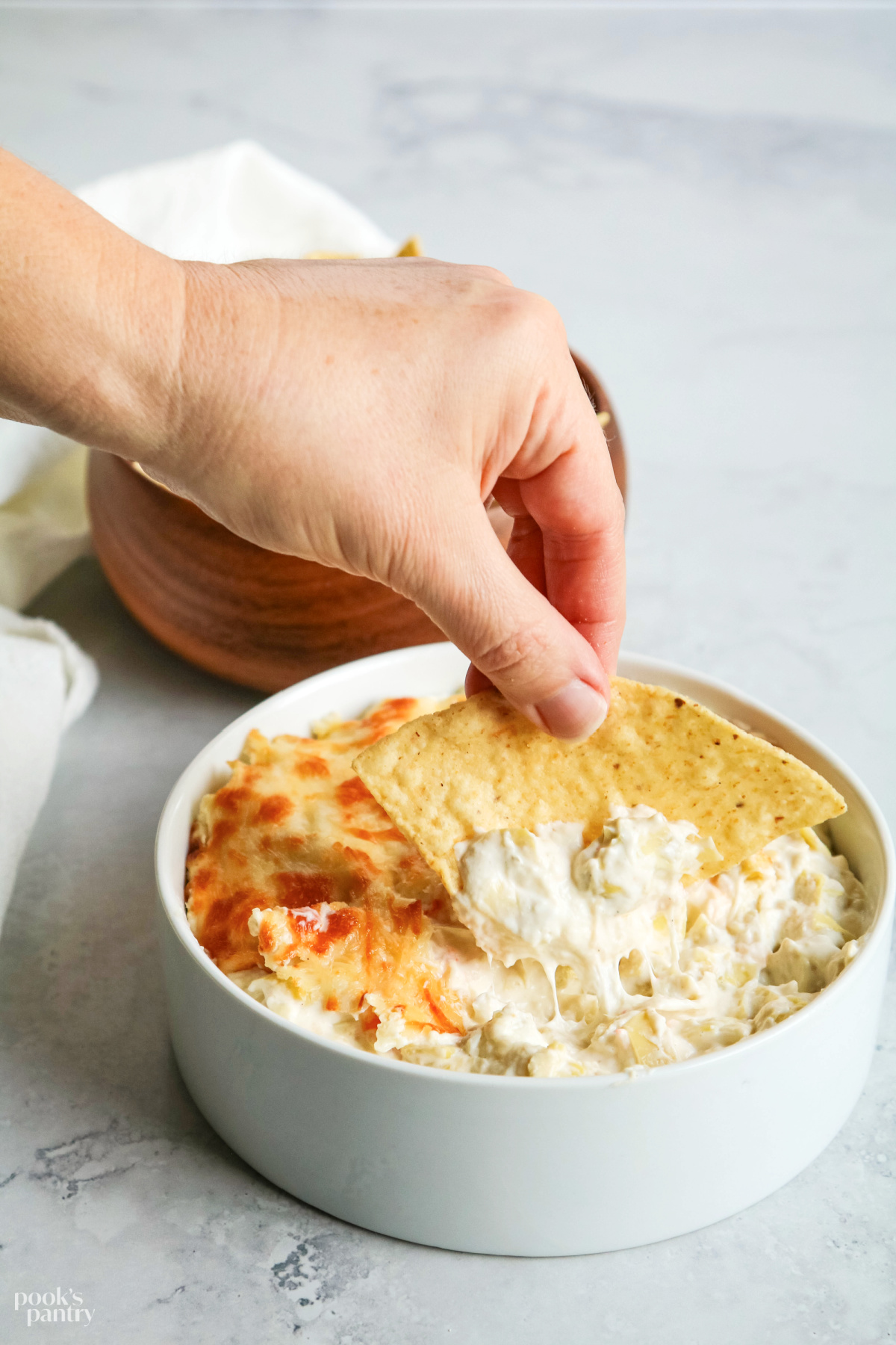 Dipping a tortilla chip into a bowl of cheesy langostino artichoke dip.