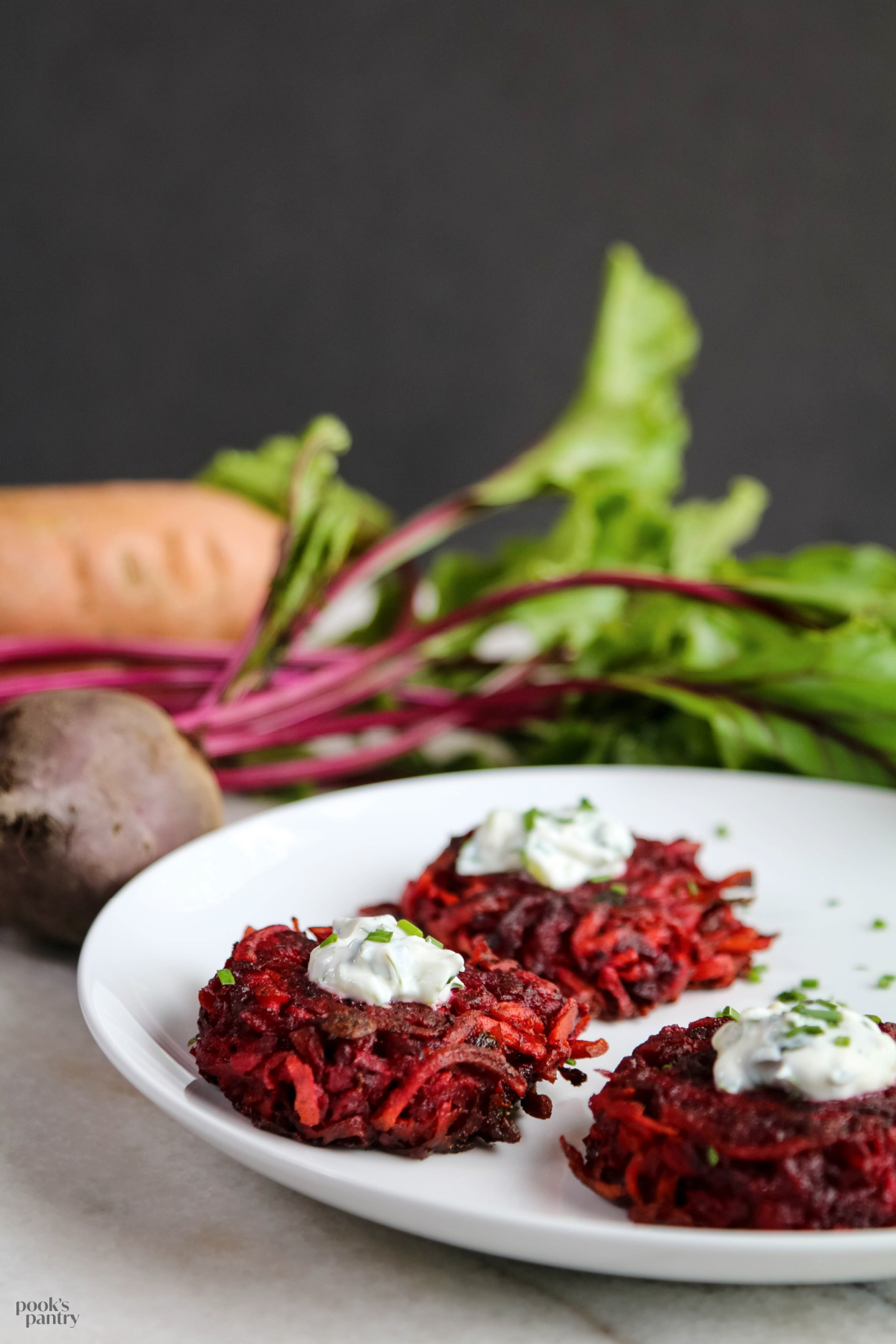 Sweet potato and beet fritters on a white plate with a dollop of sour cream and a scattering of chives on each one.