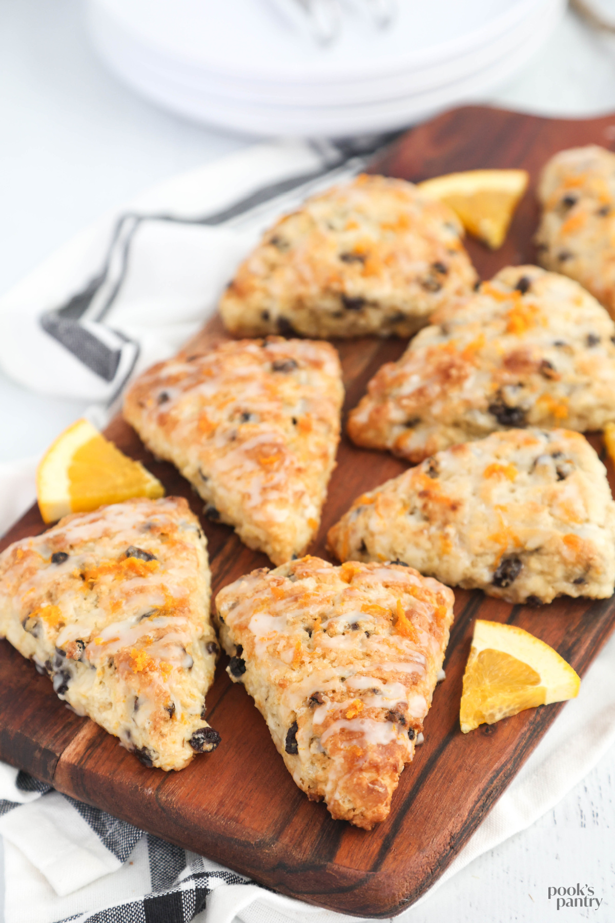 Glazed orange currant scones on a wooden board, with a black and white tea towel underneath.