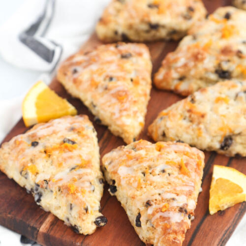 Orange currant scones with orange slices on a brown wooden cutting board, with a kitchen towel underneath.