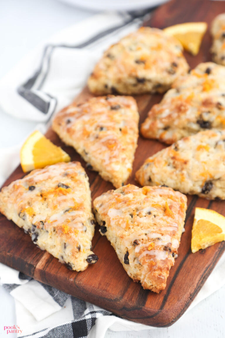 Orange currant scones with orange slices on a brown wooden cutting board, with a kitchen towel underneath.