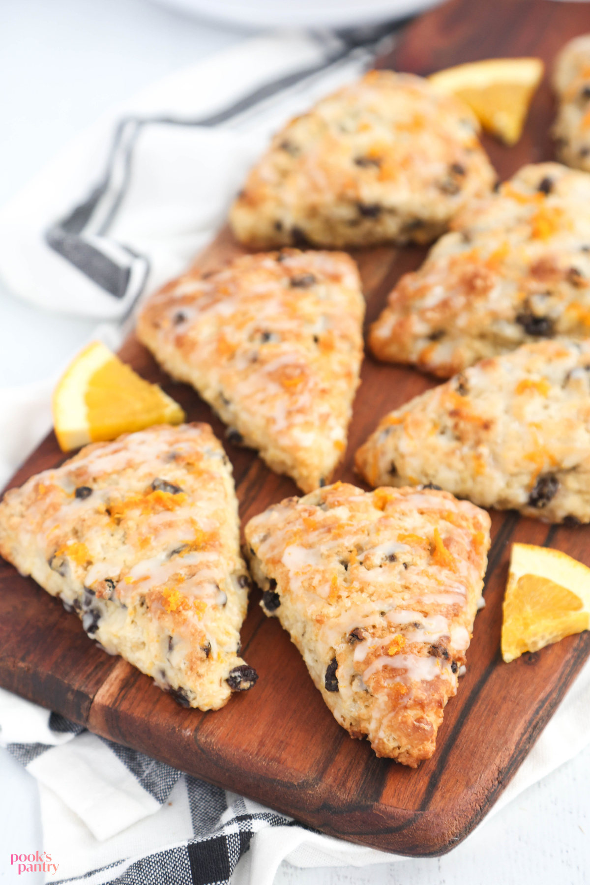 Orange currant scones with orange slices on a brown wooden cutting board, with a kitchen towel underneath.