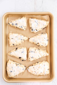 Scones topped with buttermilk on baking sheet.