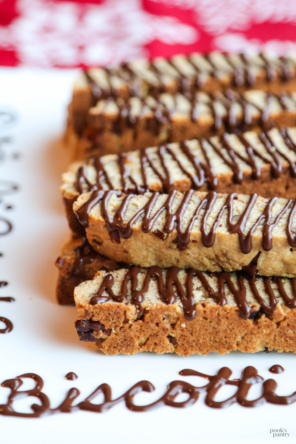 Butter pecan biscotti on a white platter with the word "biscotti" written in chocolate on the plate.