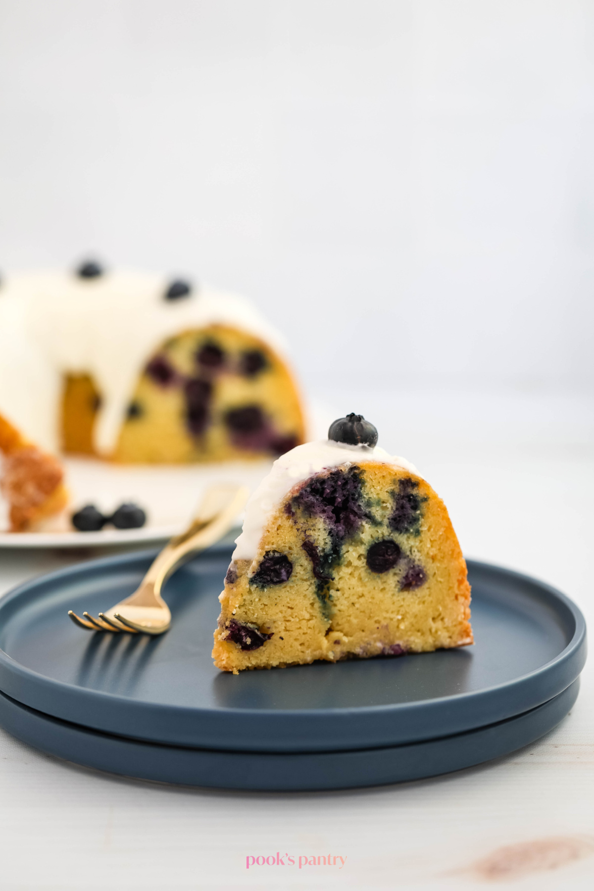 A slice of blueberry Bundt cake on a cake plate with a fork beside it.