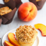 Fresh peach muffins with crumble topping on white plate.