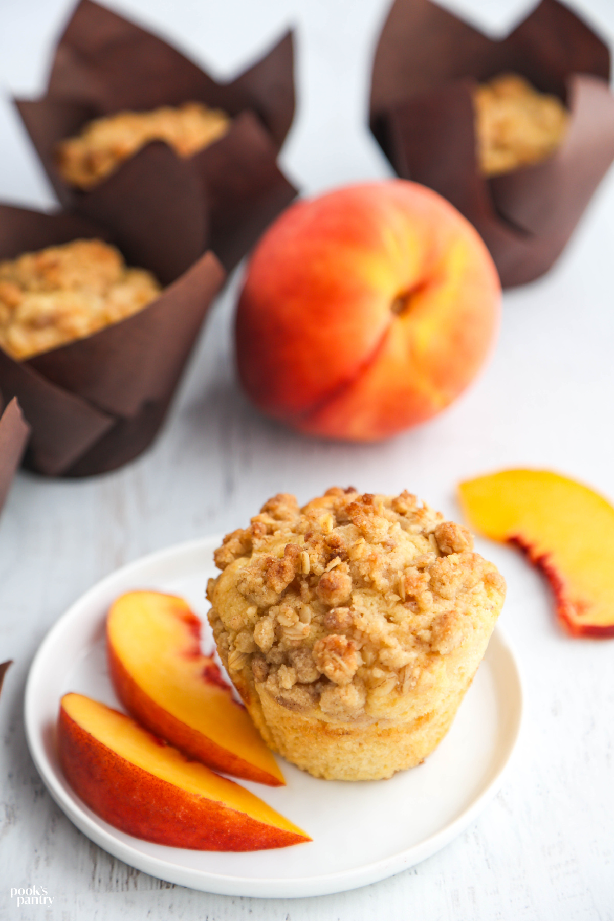 Fresh peach muffins with crumble topping on white plate.
