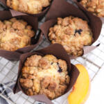 Blueberry peach muffins on a metal cooling rack with a tea towel underneath.