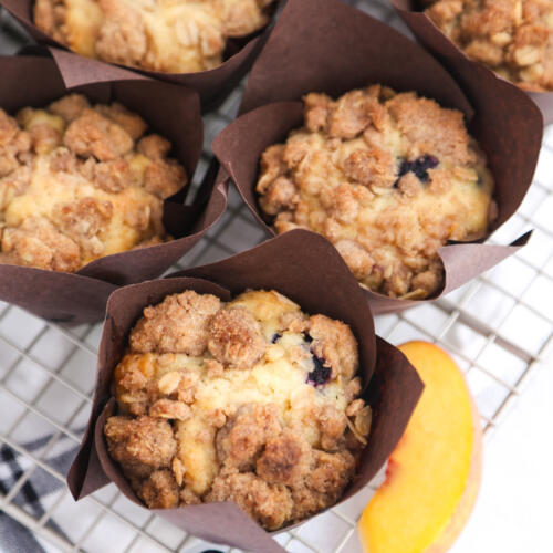 Blueberry peach muffins on a metal cooling rack with a tea towel underneath.
