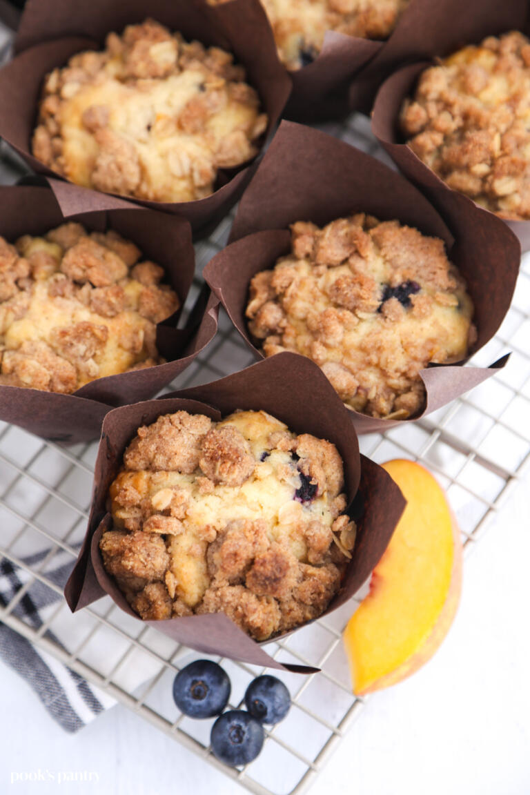 Blueberry peach muffins on a metal cooling rack with a tea towel underneath.