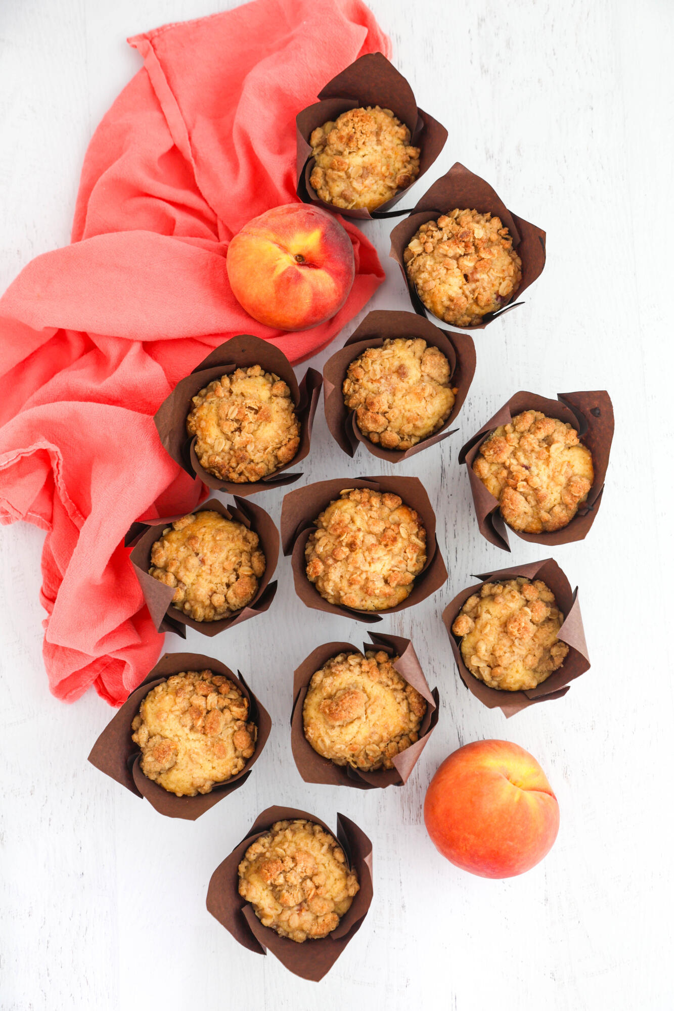 Overhead photo of peach crumble muffins with a coral tea towel on the side.